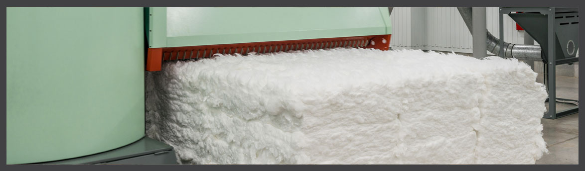 Large bale of raw cotton fiber being processed by a textile machine in an industrial facility.
