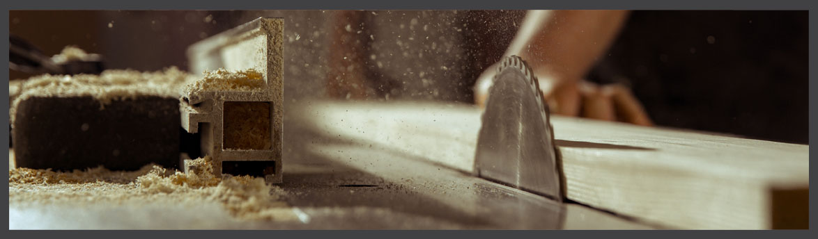 Close-up of a circular saw cutting a piece of wood with sawdust flying, in a woodworking or carpentry workshop.